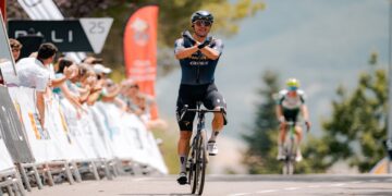 Ciclista cruza la meta celebrando con los brazos en la forma de X ante el público en Sabiñánigo